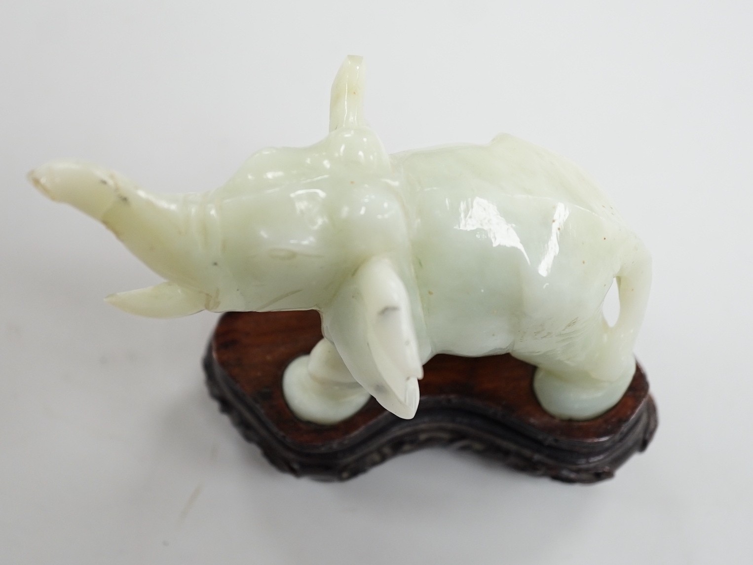 A Chinese bowenite jade elephant on hard wood stand, 11cm tall